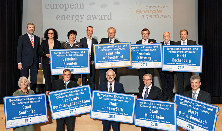 Die Vertreter der ausgezeichneten Kommunen mit den Gratulanten. Hintere Reihe von links: Dr. Marcel Huber (damaliger Staatsminister für Umwelt und Verbraucherschutz), Prof. Dr.-Ing. Lamia Messari-Becker (Universität Siegen), Michaela Waldmann (1. Bürgermeisterin von Pfronten), Martin Sambale (eza!-Geschäftsführer), Arno Zengerle (1. Bürgermeister von Wildpoldsried), Christian Schlegel (1. Bürgermeister von Stöttwang), Dr. Armand Dütz (Geschäftsführer der eea-Bundesgeschäftsstelle), Toni Barth (1. Bürgermeister von Buchenberg). Vordere Reihe von links: Ingrid Fischer (3. Bürgermeisterin von Sonthofen), Rudolf Schaupp (stellvertretender Landrat Landkreis Berchtesgadener Land), Jörg Fischer (Bürgermeister von Donauwörth), Dr. Stefan Winter (1. Bürgermeister von Mindelheim), Bernhard Kerler (1. Bürgermeister von Bad Grönenbach).Bild: eza! Die Vertreter der ausgezeichneten Kommunen mit den Gratulanten. Hintere Reihe von links: Dr. Marcel Huber (damaliger Staatsminister für Umwelt und Verbraucherschutz), Prof. Dr.-Ing. Lamia Messari-Becker (Universität Siegen), Michaela Waldmann (1. Bürgermeisterin von Pfronten), Martin Sambale (eza!-Geschäftsführer), Arno Zengerle (1. Bürgermeister von Wildpoldsried), Christian Schlegel (1. Bürgermeister von Stöttwang), Dr. Armand Dütz (Geschäftsführer der eea-Bundesgeschäftsstelle), Toni Barth (1. Bürgermeister von Buchenberg). Vordere Reihe von links: Ingrid Fischer (3. Bürgermeisterin von Sonthofen), Rudolf Schaupp (stellvertretender Landrat Landkreis Berchtesgadener Land), Jörg Fischer (Bürgermeister von Donauwörth), Dr. Stefan Winter (1. Bürgermeister von Mindelheim), Bernhard Kerler (1. Bürgermeister von Bad Grönenbach).Bild: eza!