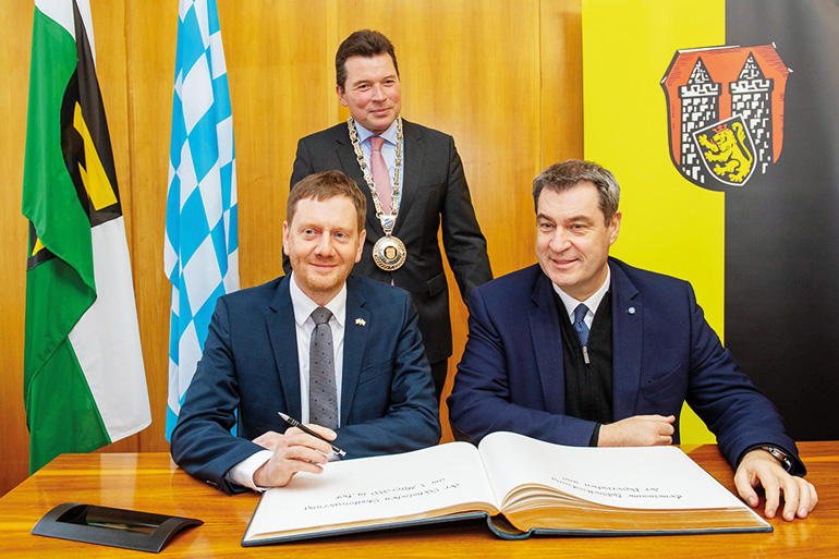 Sachsens Ministerpräsident Michael Kretschmer (links) und Bayerns Ministerpräsident Dr. Markus Söder, MdL (rechts), tragen sich im Beisein des Oberbürgermeisters der Stadt Hof, Dr. Harald Fichtner (Mitte), in das Gästebuch der Stadt Hof ein. Bild: Bayerische Staatskanzlei