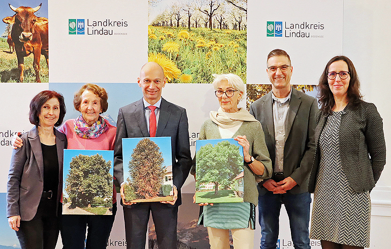 Landrat Elmar Stegmann zeichnet Gina Jäckel und ihre Linde mit dem ersten Preis aus. Der zweite Preis geht an Rosa Asmussen und ihren Walnussbaum. Theophil Pflaum und seine Araucaria werden mit dem dritten Preis geehrt. Der Landrat zeigt ein Foto des drittplatzierten Baumes – Theophil Pflaum konnte nicht zur Preisverleihung kommen. Gemeinsam mit dem Landrat und den Preisträgerinnen freuen sich Bernd Brunner, Kreisfachberater für Gartenkultur und Landespflege sowie Dr. Julia Lorenzen und Hildegard Nagler vom Heimatkundlichen Dokumentationszentrum des Landkreises Lindau. V.l.: Hildegard Nagler, Gina Jäckel, Landrat Elmar Stegmann, Rosa Asmussen, Bernd Brunner und Dr. Julia Lorenzen. Bild: Landkreis Lindau/Nadja Krassik