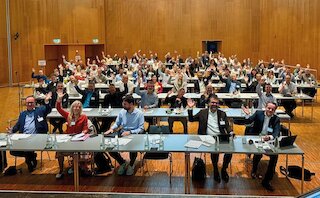 Foto eines Raumes mit Personen anTischen