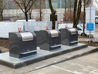 Unterirdisches Entsorgungssystem mit Betonbehälter im Erdreich: Ein Müllcontainer wird per Kranfahrzeug zur Entleerung angehoben, automatische Sicherheitsplattform verhindert Unfälle.