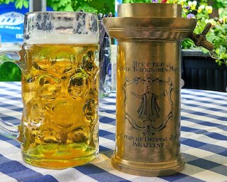 Ein Liter Bier im Maßkrug und die „Mutter einer bayerischen Maß“. Das Gefäß diente zum Eichen einer bayerischen Maß und fasste 1,069 preußische Liter Bier. Eingeschenkt wurde bis zur Oberkante; überschüssiges Bier lief über den Hahn wieder ab.